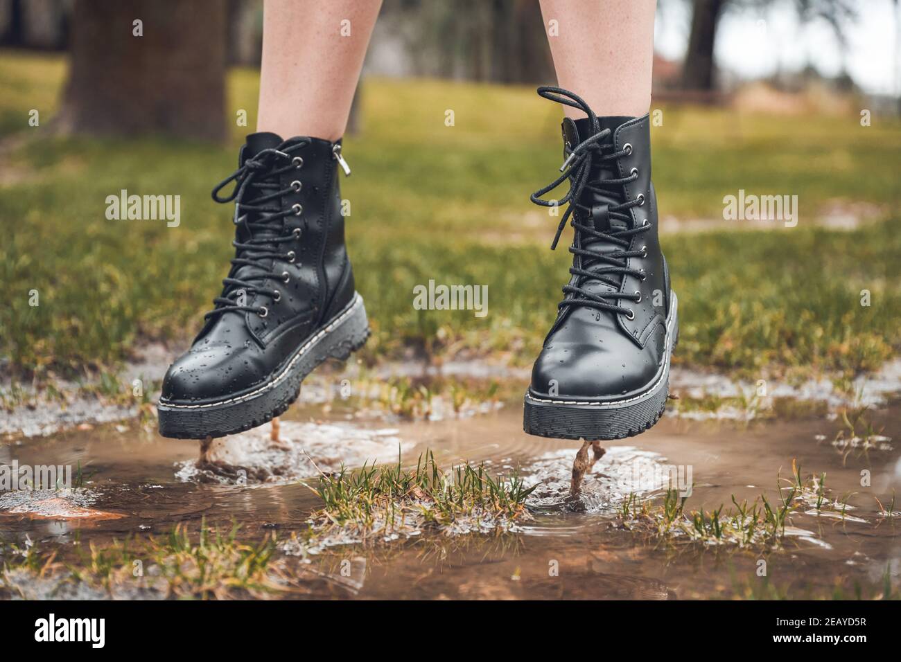 Selective focus shot of a lady wearing black ankle boots jumping over a puddle in a park Stock Photo