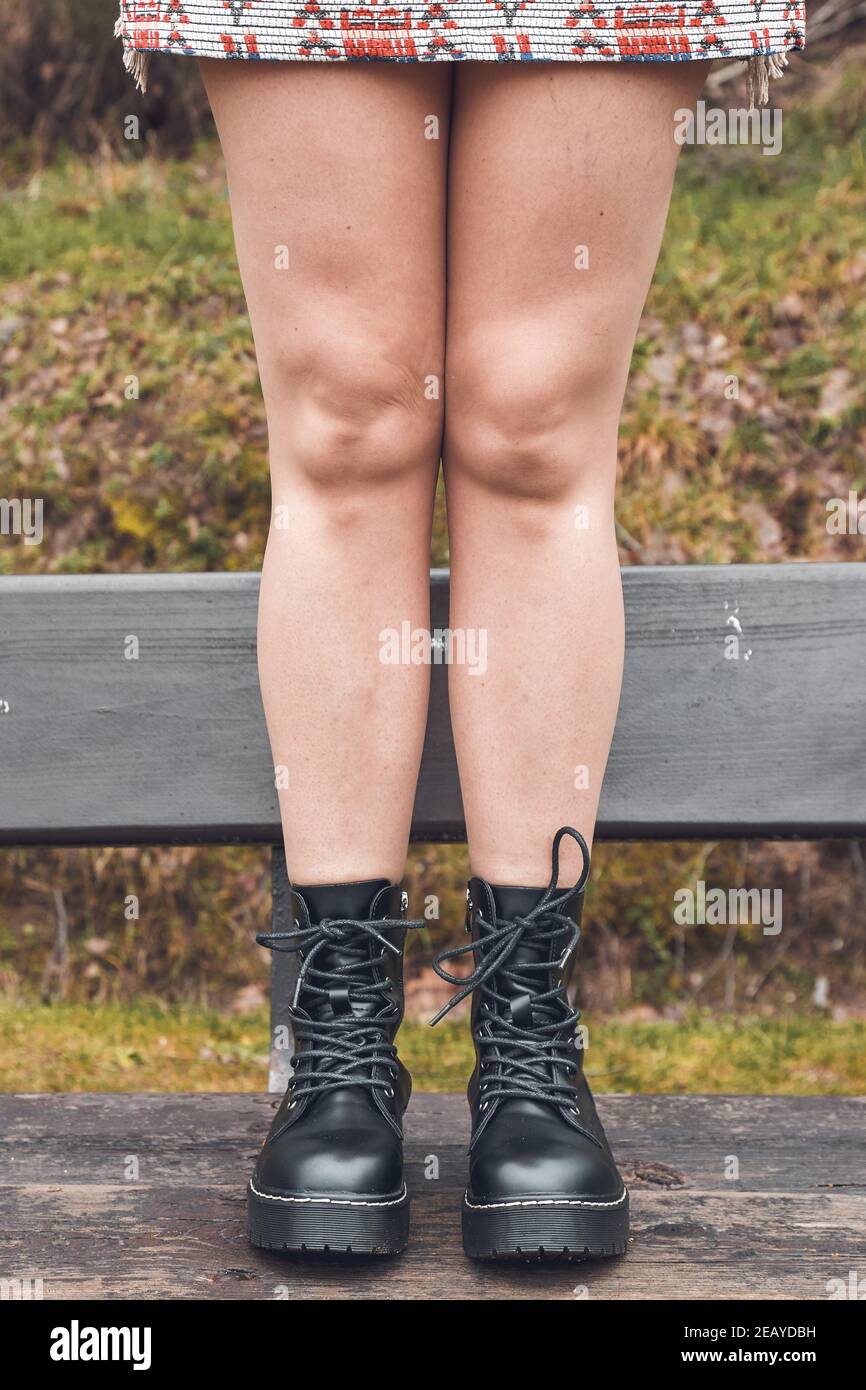 Vertical shot of a lady's legs wearing a skirt with black ankle boots standing on a bench Stock Photo