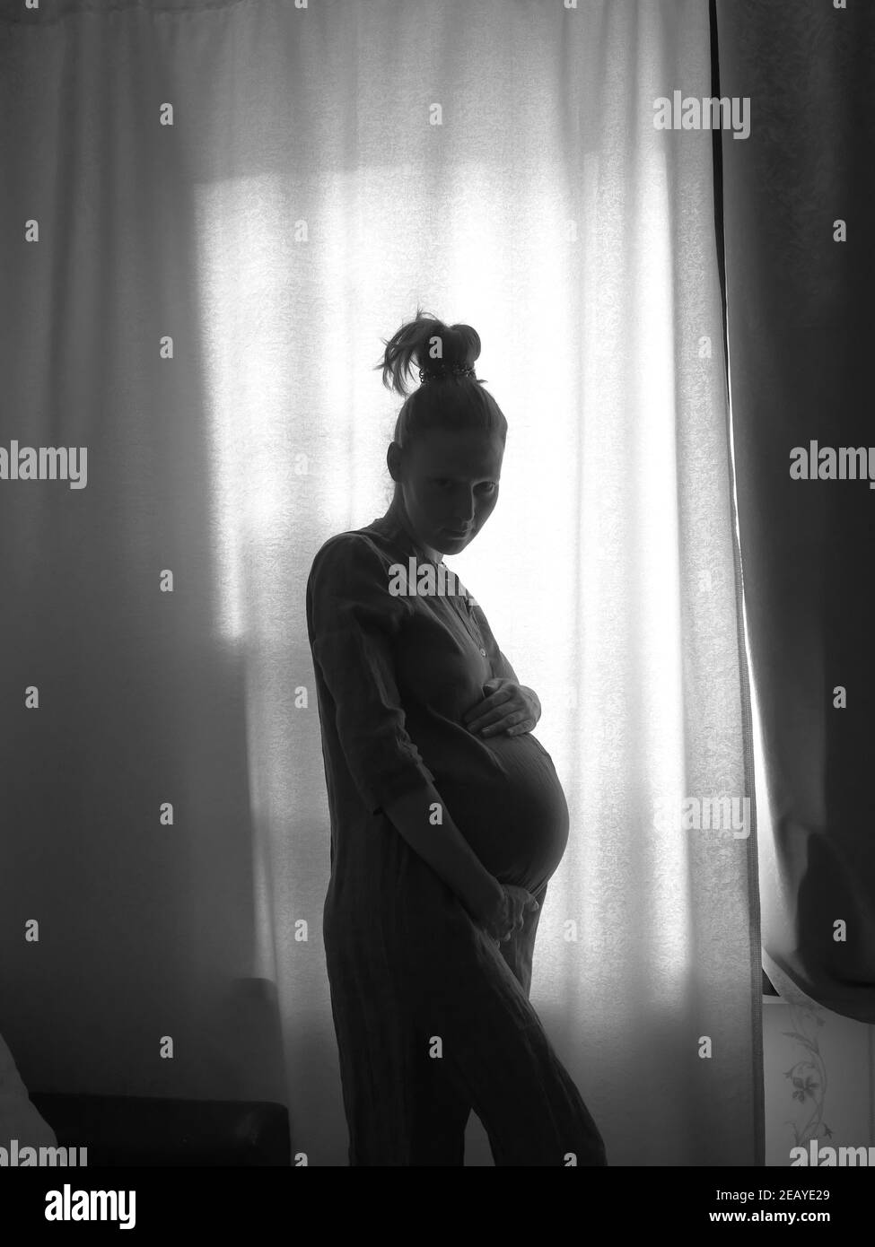 The silhouette of a pregnant girl standing by the window. Black and white photo. Stock Photo