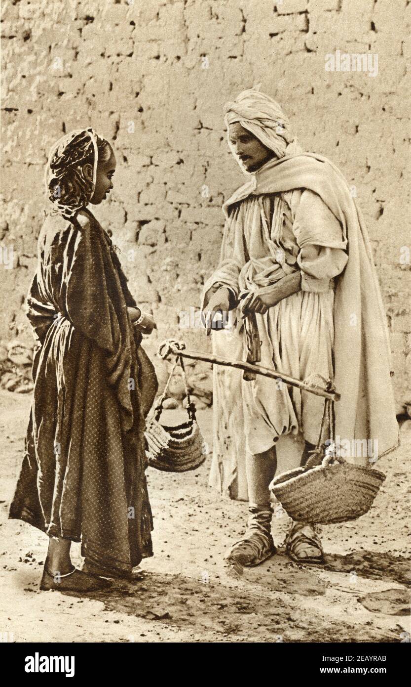 An early 20th century photo of an Algerian trader weighing out vegetables to a customer circa 1920 Stock Photo