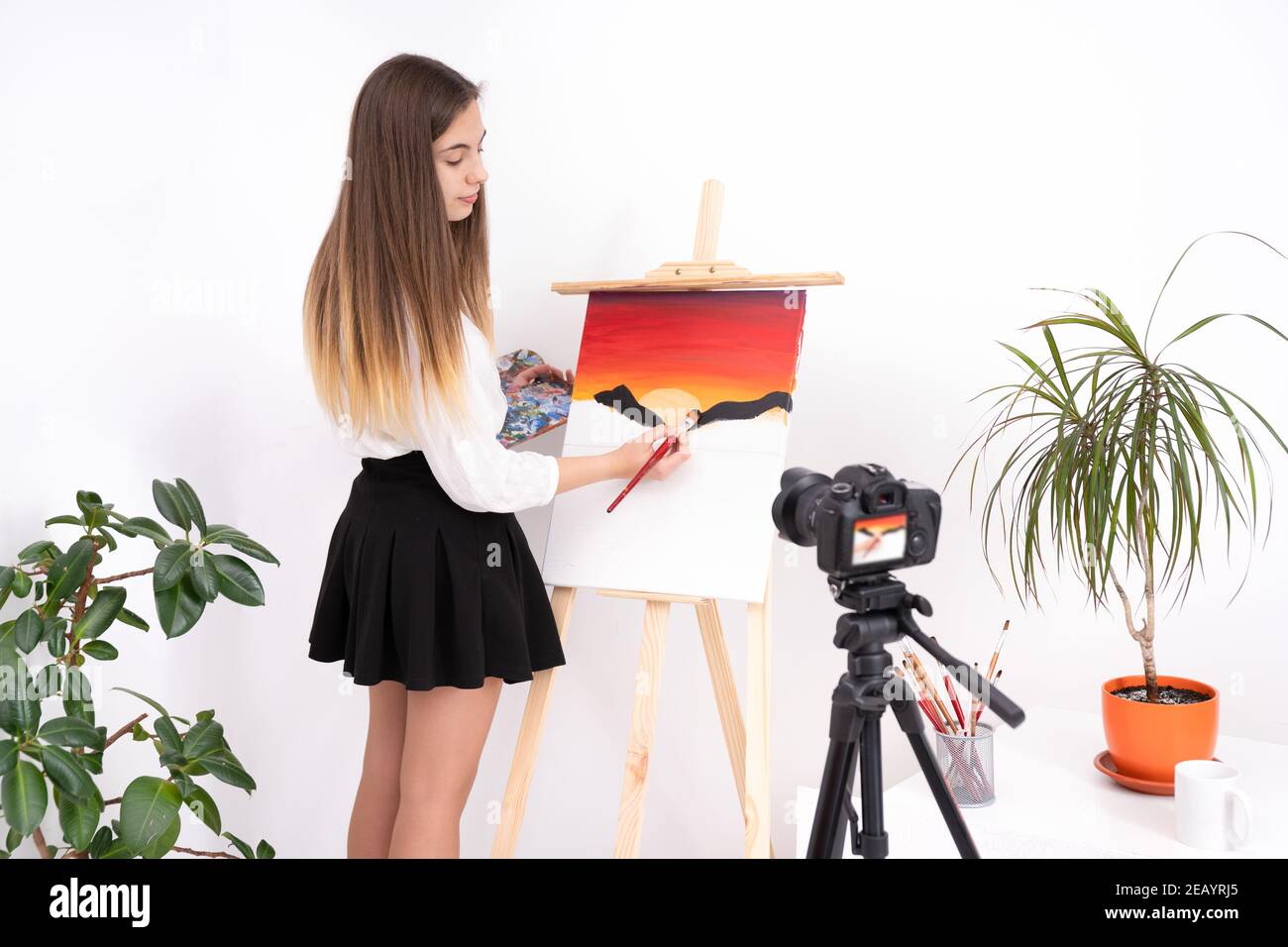 Beautiful young lady in an art studio painting on canvas with a brush ...