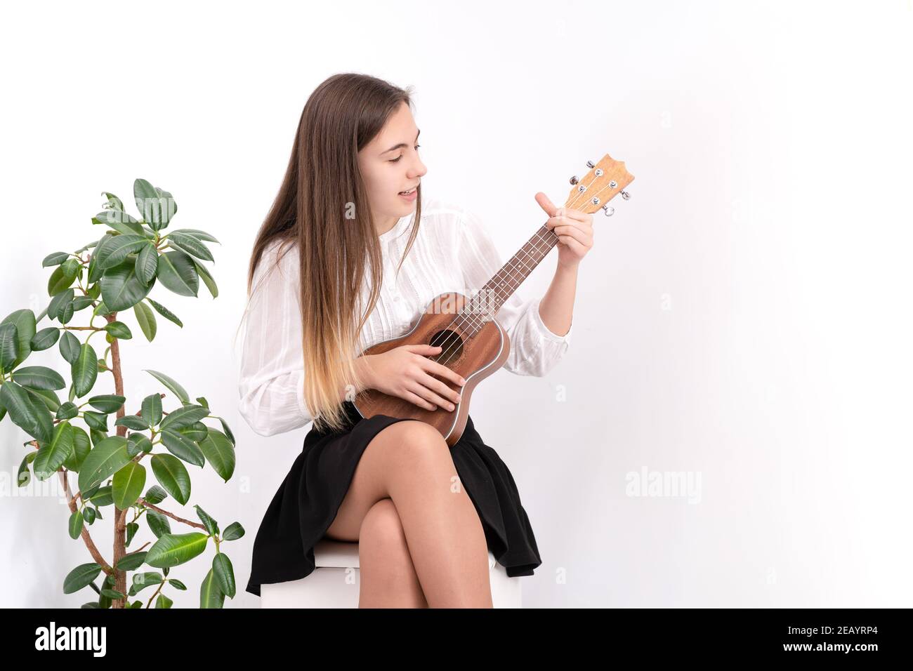 Beautiful young lady sitting playing the ukulele wearing a white blouse and  a black skirt Stock Photo - Alamy