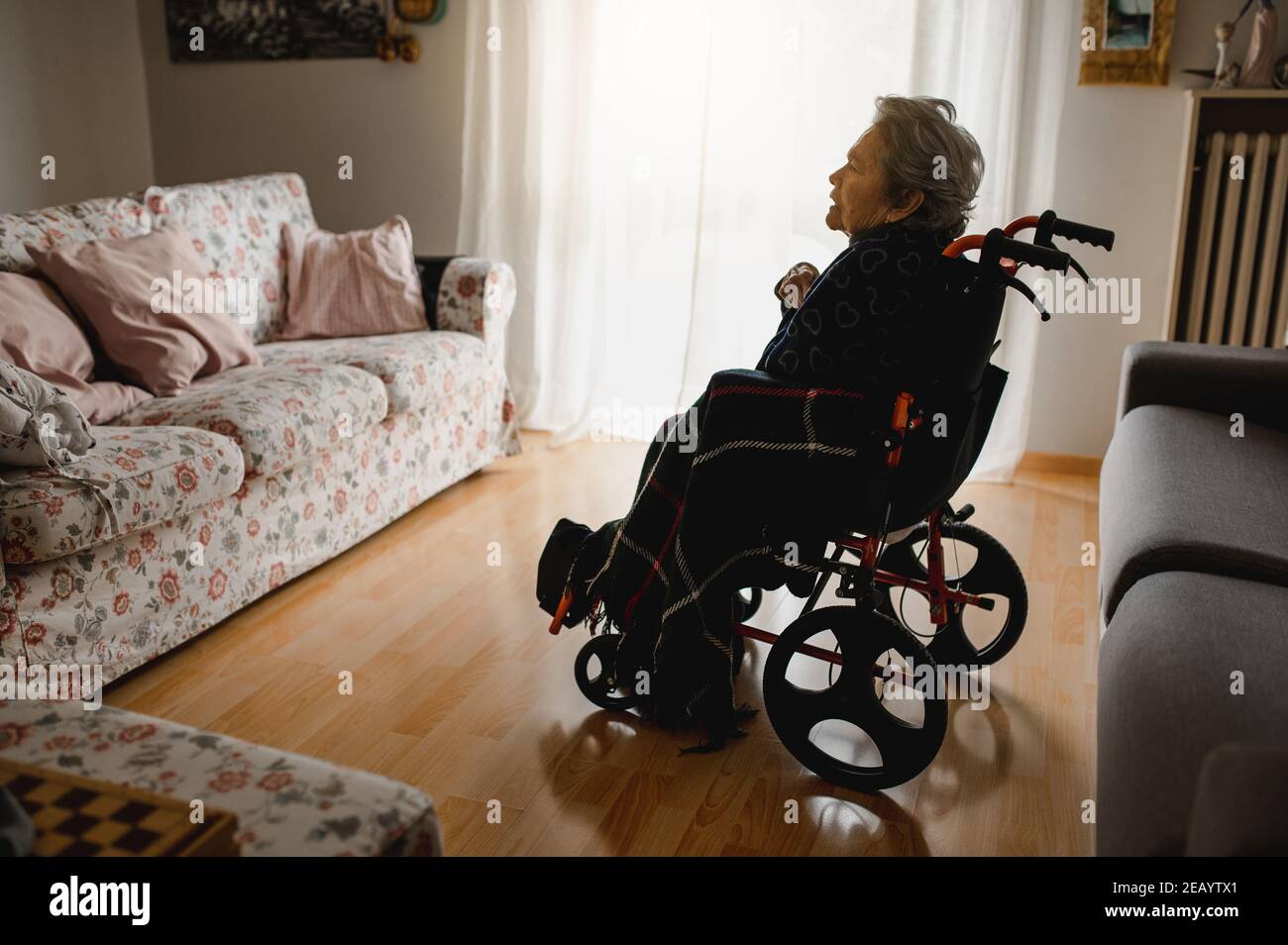 Old sick woman in wheelchair in the middle of domestic room alone Stock Photo