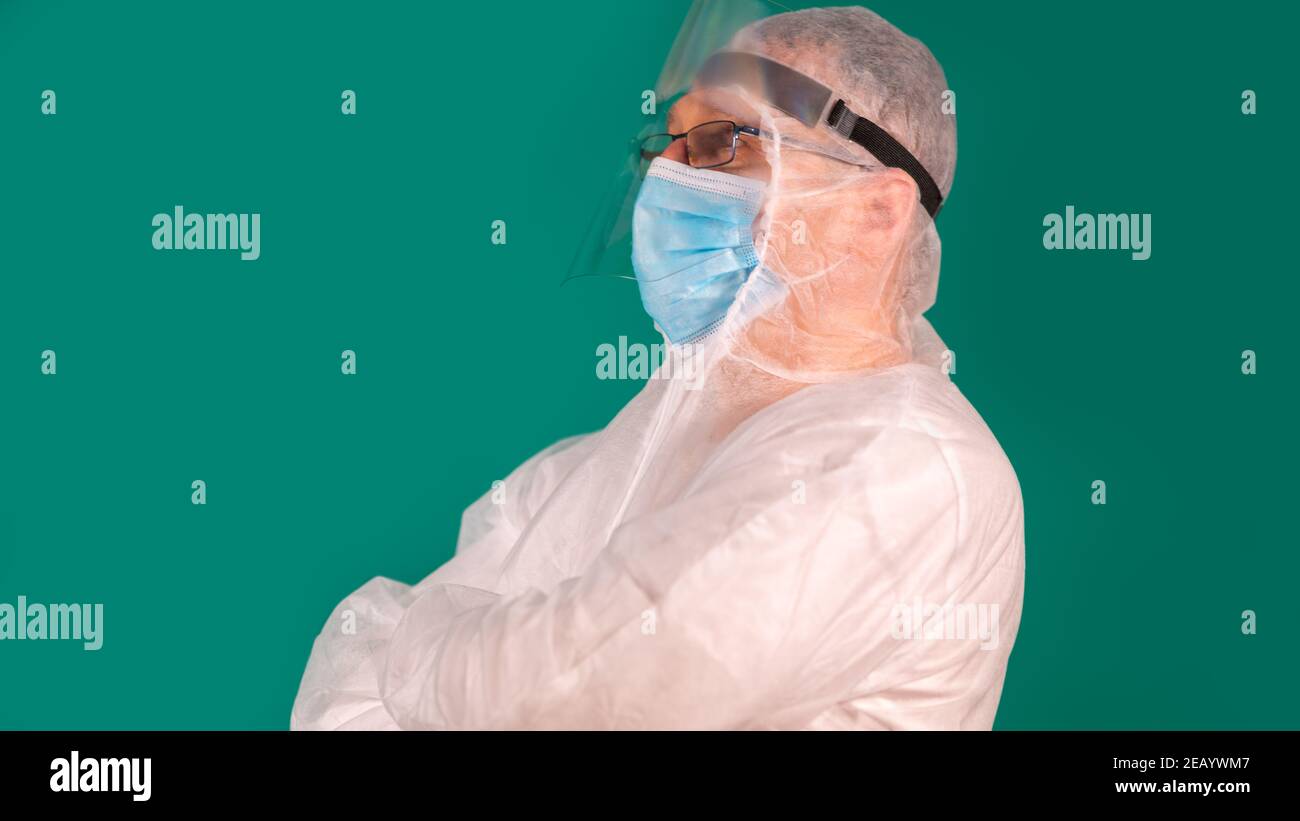 Male doctor in PPE suit uniform standing sideways with arms crossed Stock Photo