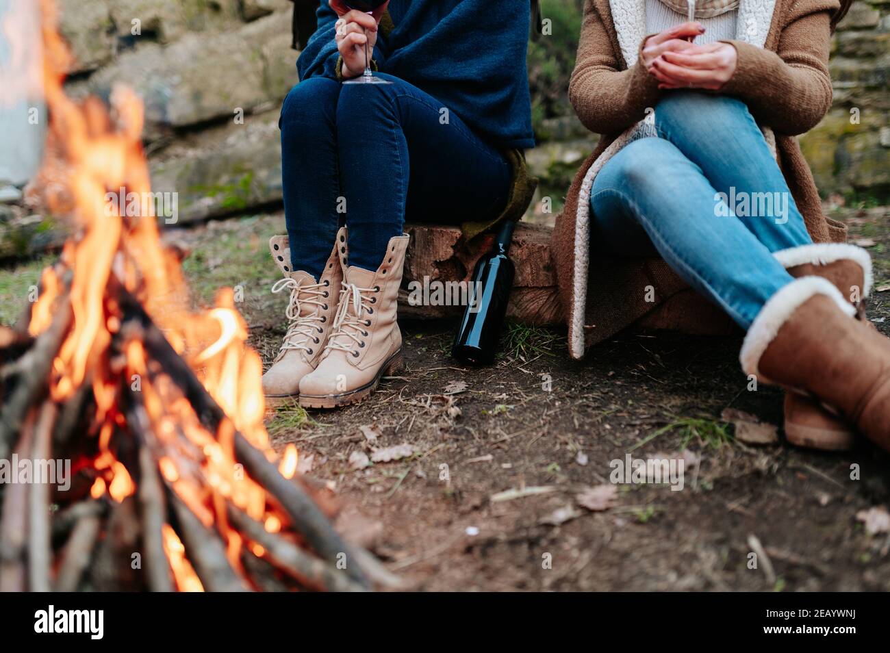 Unrecognizable women holding glass of red wine in campfire warming next to a fire. Stock Photo