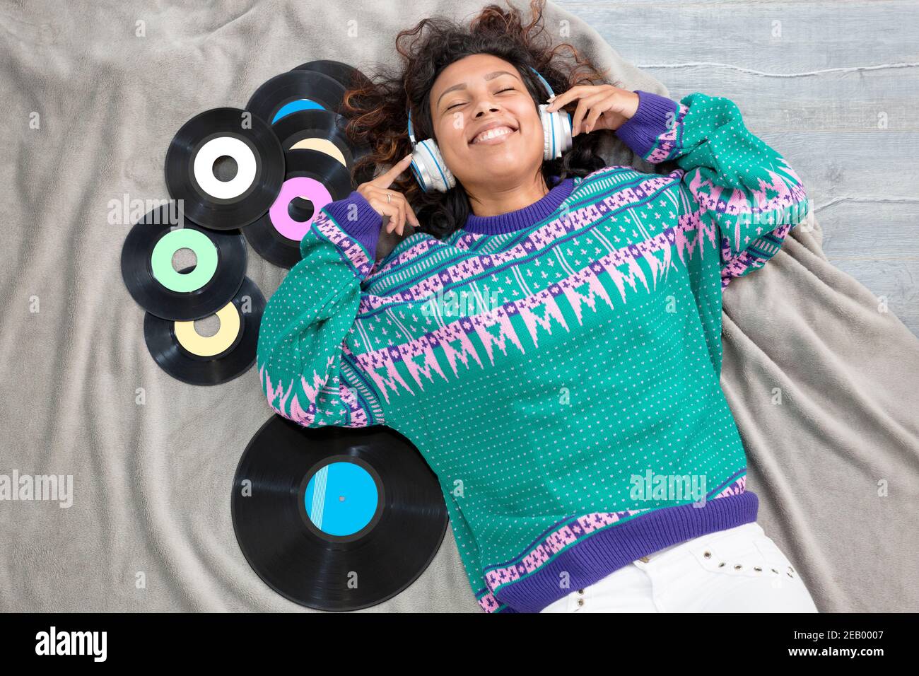 Top view of Latin girl lying on the floor listening to music with vinyl records around her. Stock Photo