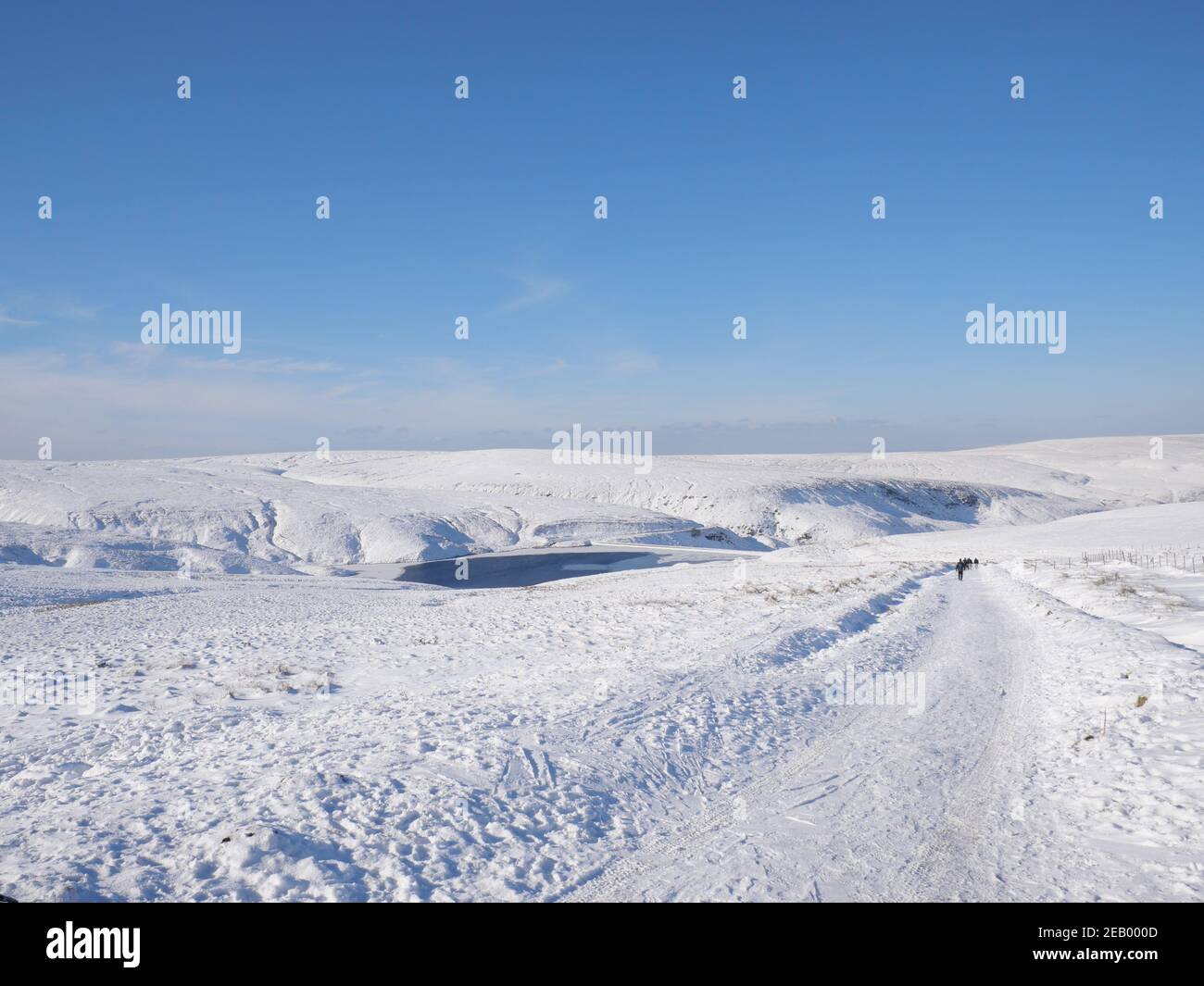 Snow covered moorland Pennine Way footpath with frozen reservoir and blue sky Stock Photo