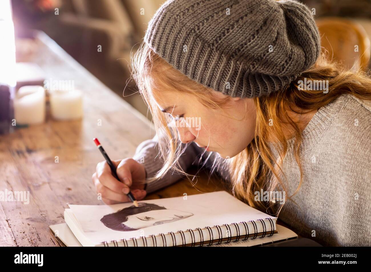 Teenage girl in a woolly hat drawing with a pencil on a sketchpad. Stock Photo