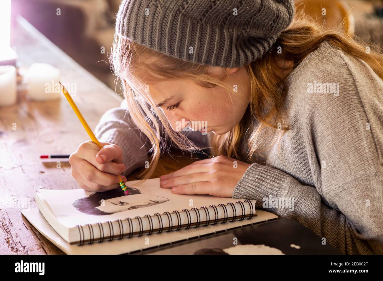 Teenage girl in a woolly hat drawing with a pencil on a sketchpad. Stock Photo