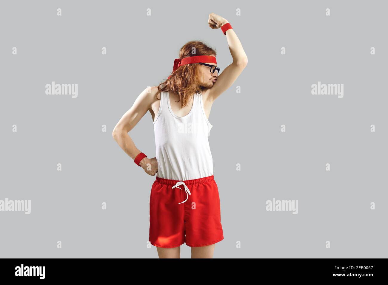 Funny skinny nerd in tank top and shorts kissing weak biceps after first sports workout Stock Photo