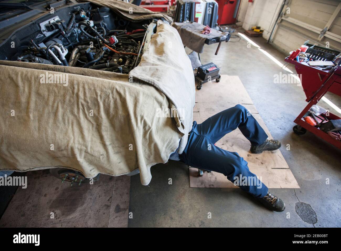 Mechanic lays on a trolley under a car in an auto repair shop Stock
