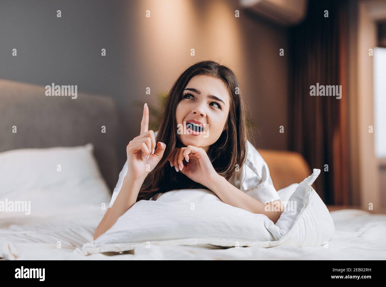 Young beautiful woman has an idea while she is lying on the bed. The female model shows emotions Stock Photo