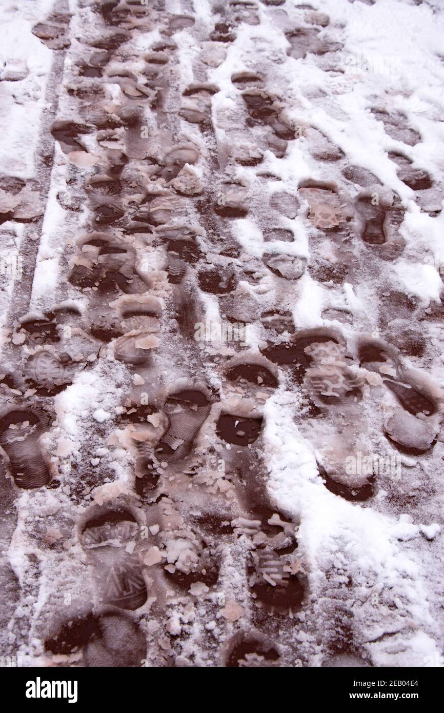 Footprints on melting snow covered red sidewalk pavement. Safety issue