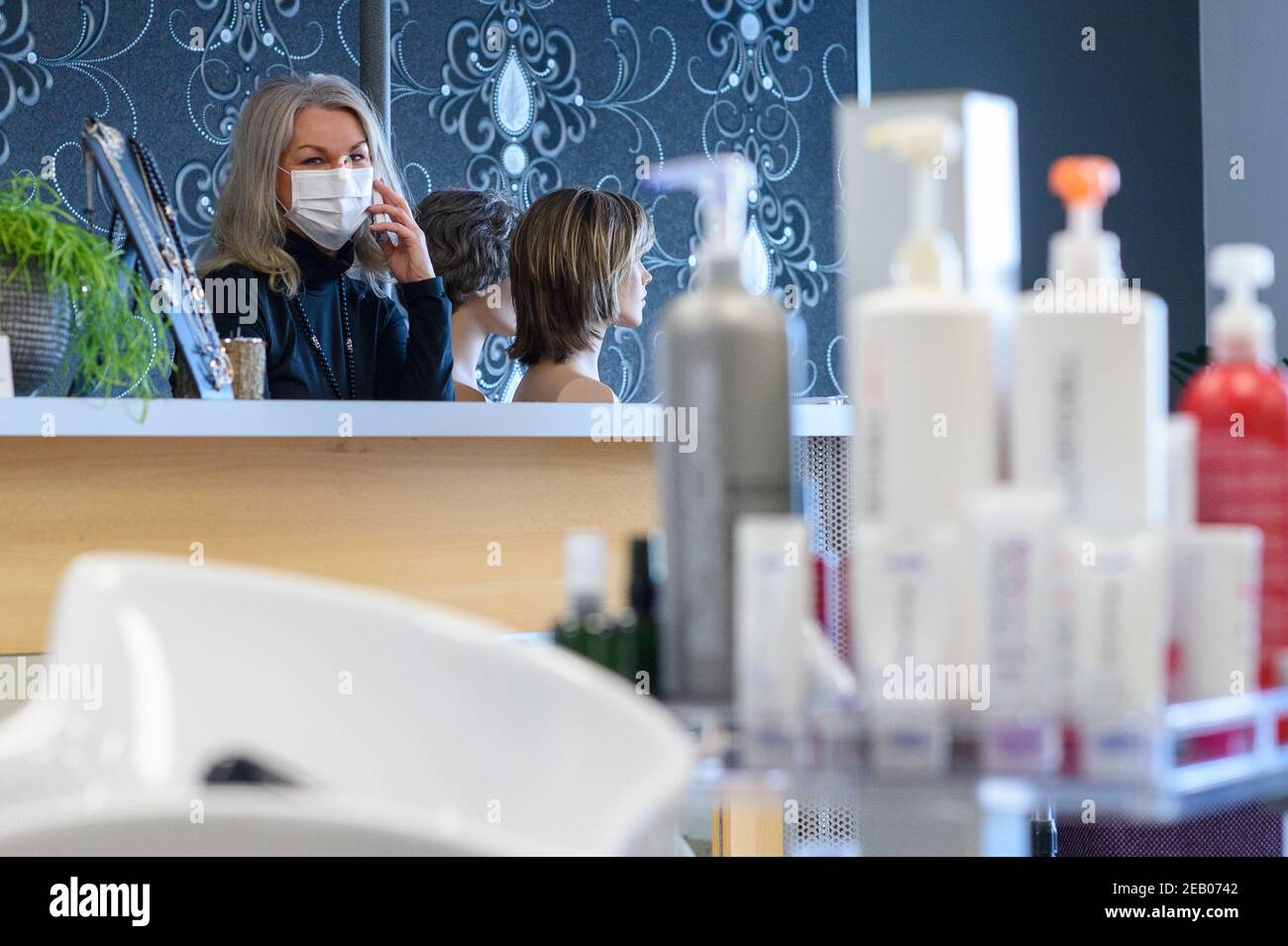 Magdeburg, Germany. 11th Feb, 2021. Antje Raschbacher, master hairdresser  and owner of the hair salon "Die Haarschneider", stands behind the  reception counter and talks to customers on the phone. The owners had