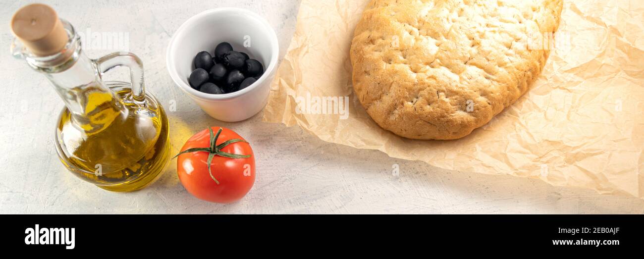 Banner with Italian focaccia or Italian bread. Fresh, tasty bread with aromatic herbs on wooden board next to tomato, black olives and olive oil with Stock Photo