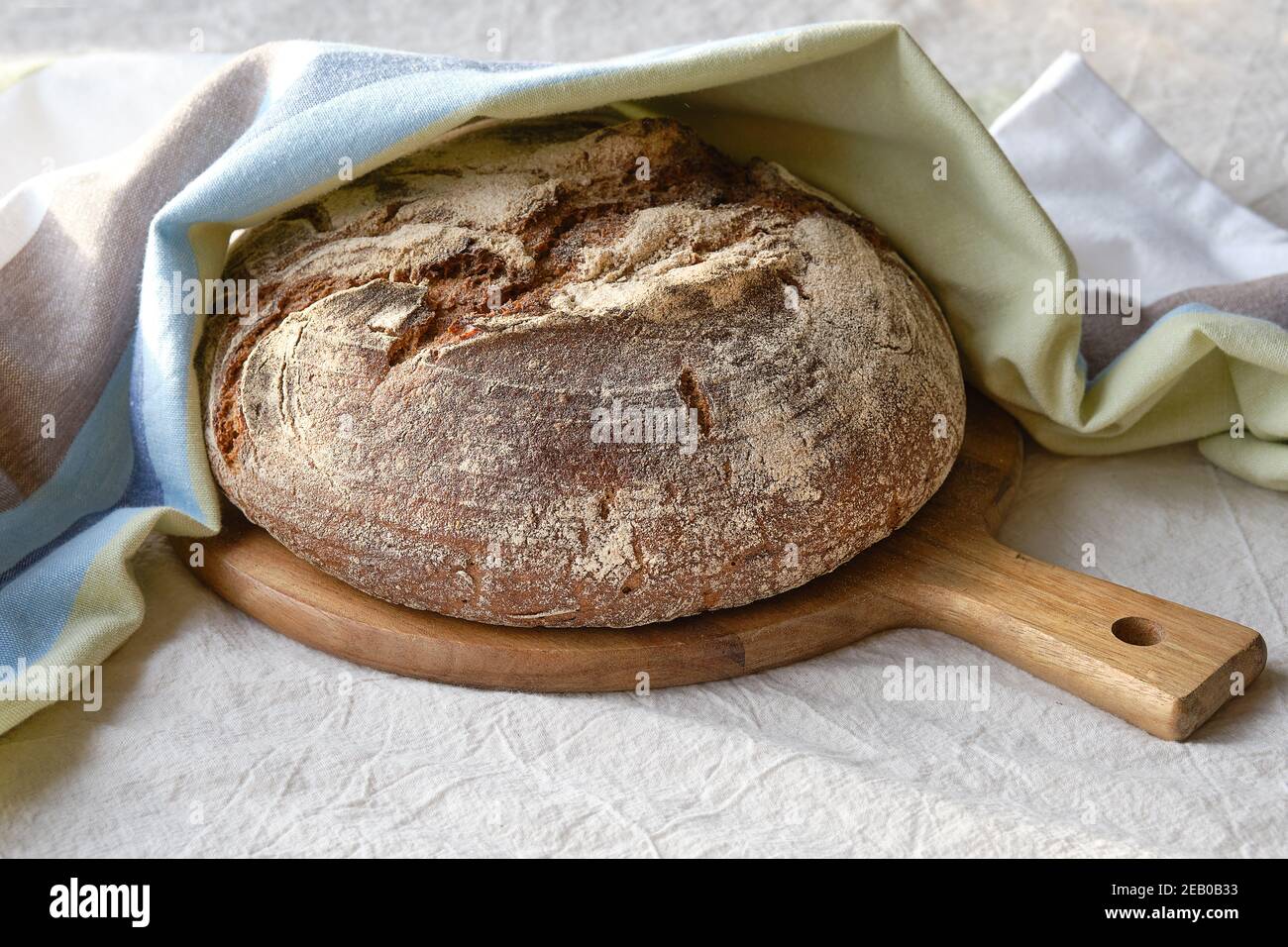 No knead handmade loaf on cutting board. German Bauernbrot means Farmers Bread in English. Wholemeal rye wheat bread baked in ceramic pan at home. Stock Photo