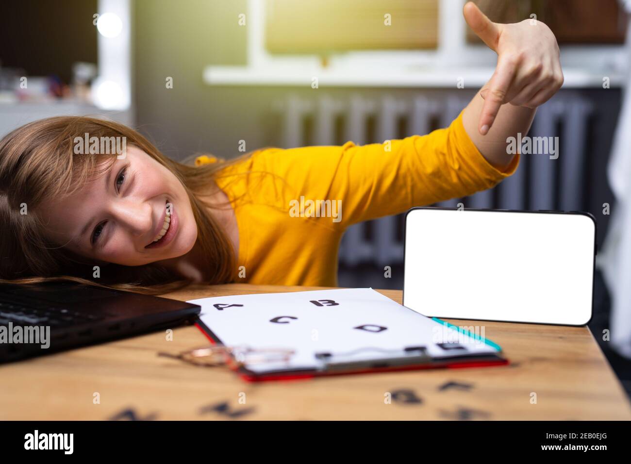 Online education concept. A young blonde girl shows a forefinger on a white sheet with black letters smiles and looks into the camera. Stock Photo
