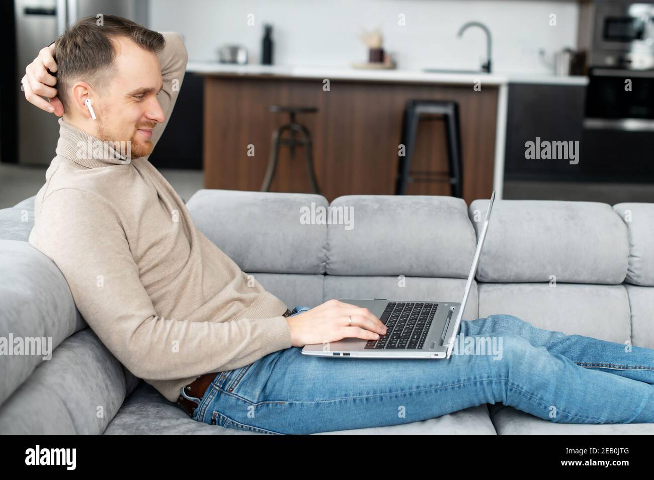 Side view a guy is using laptop lying on the comfortable couch, a young man watching movies, web surfing, play video games. A freelancer is works Stock Photo