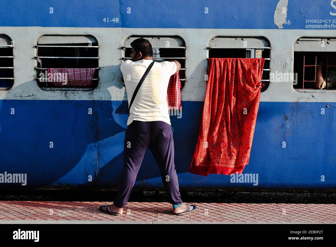 Kanyakumari, Tamil Nadu, India - Januray, 2017: Man standing on the railway platform near train and looking in window. Colorful sari drying and waving Stock Photo