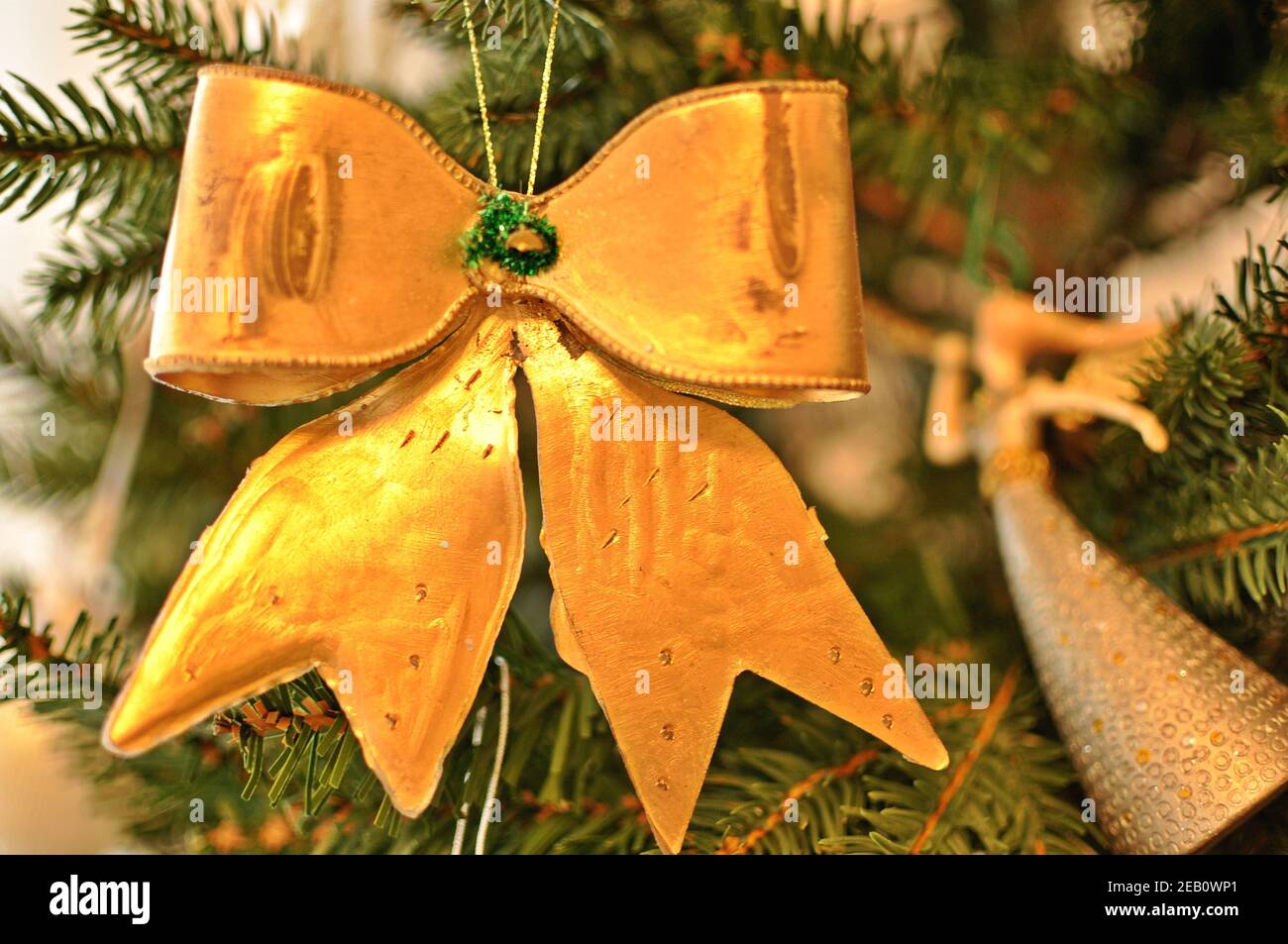Golden Christmas decoration hanging on a branch in the green tree, in form of bow (knot) with soft bokeh. Close up, front view Stock Photo