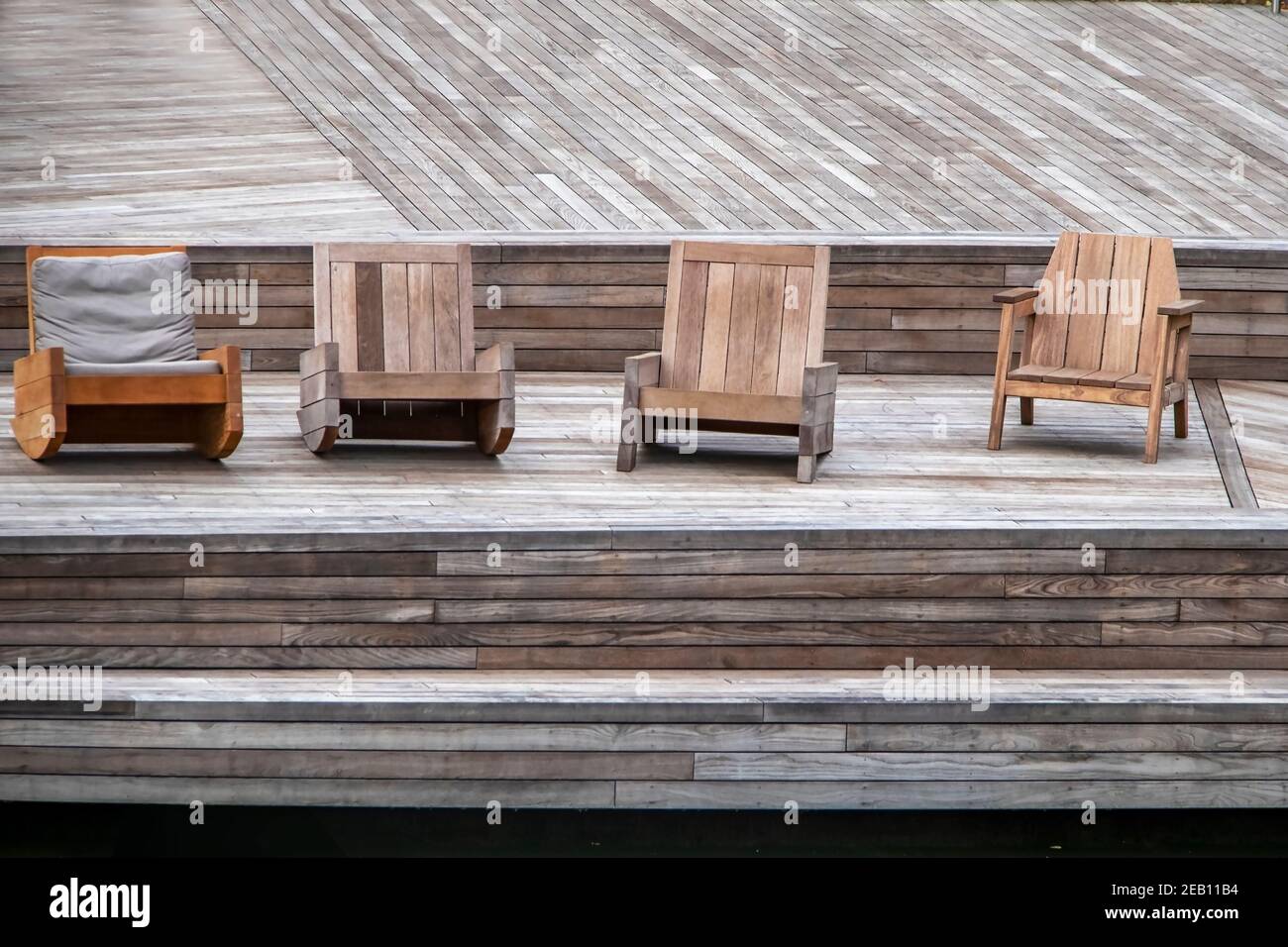 Beauty in Wood - Assorted comfy wooden chairs sit on a wooden deck at waterside Stock Photo