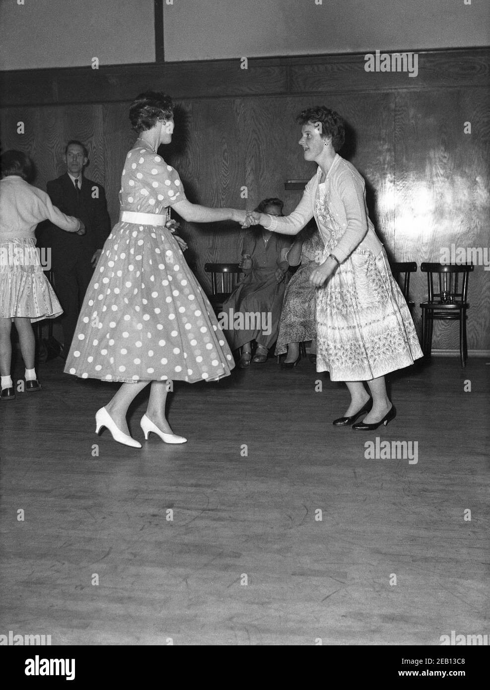 1950s, historical, 'doing the twist', at a birthday party, inside a large hotel room, two young women, one wearing a fashionable spotted or polka dot dress, having a dance together on a wooden floor, England, UK. In Britain it was still the era of swing, of the big band and swing movement but musically there were changes coming and the emerging skiffle sound and the rockabilly were just around the corner. Stock Photo