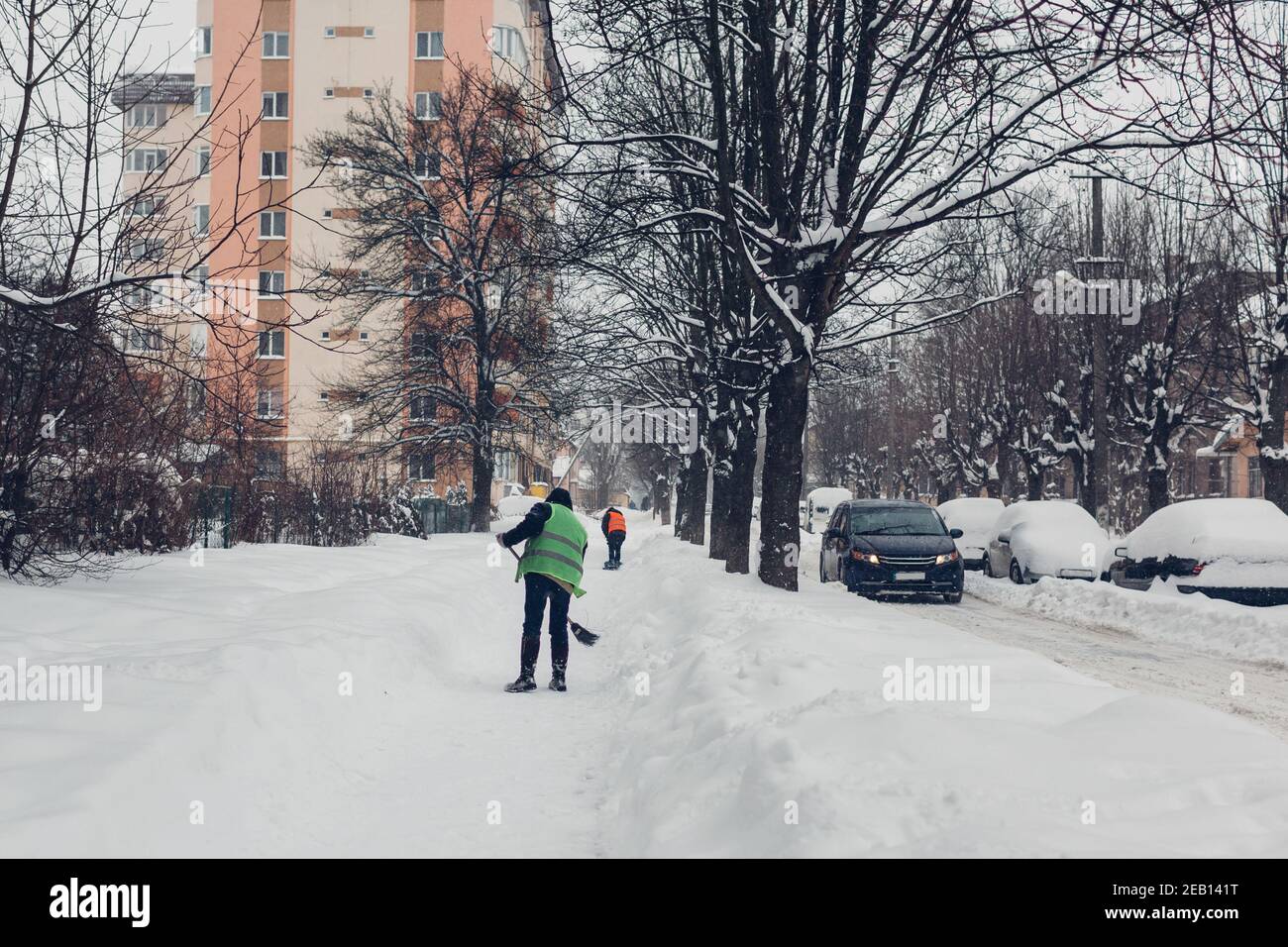 Workers cleaning pavements on city street from snow using shovel and