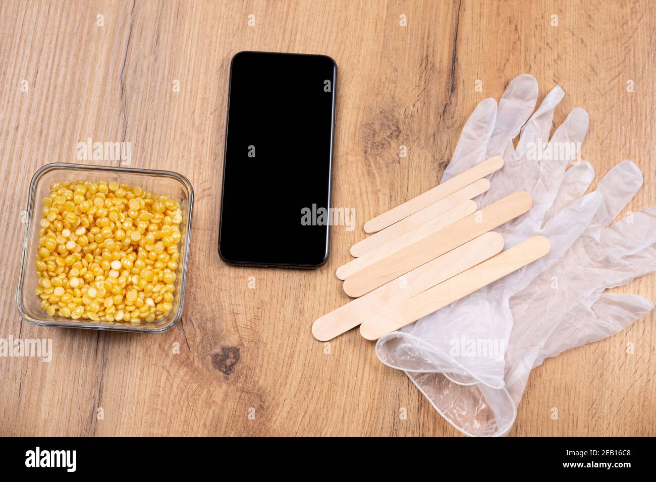 Mock up screen smartphone near depilation waxing set: spatula, medical gloves and pearl wax granules on wooden table background. Technology and beauty Stock Photo