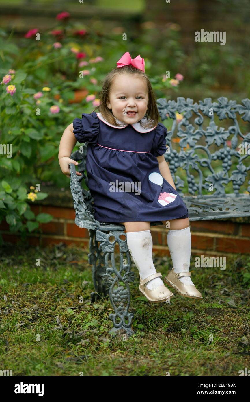 A toddler little girl with a navy dress and pink bow is sitting on an ...