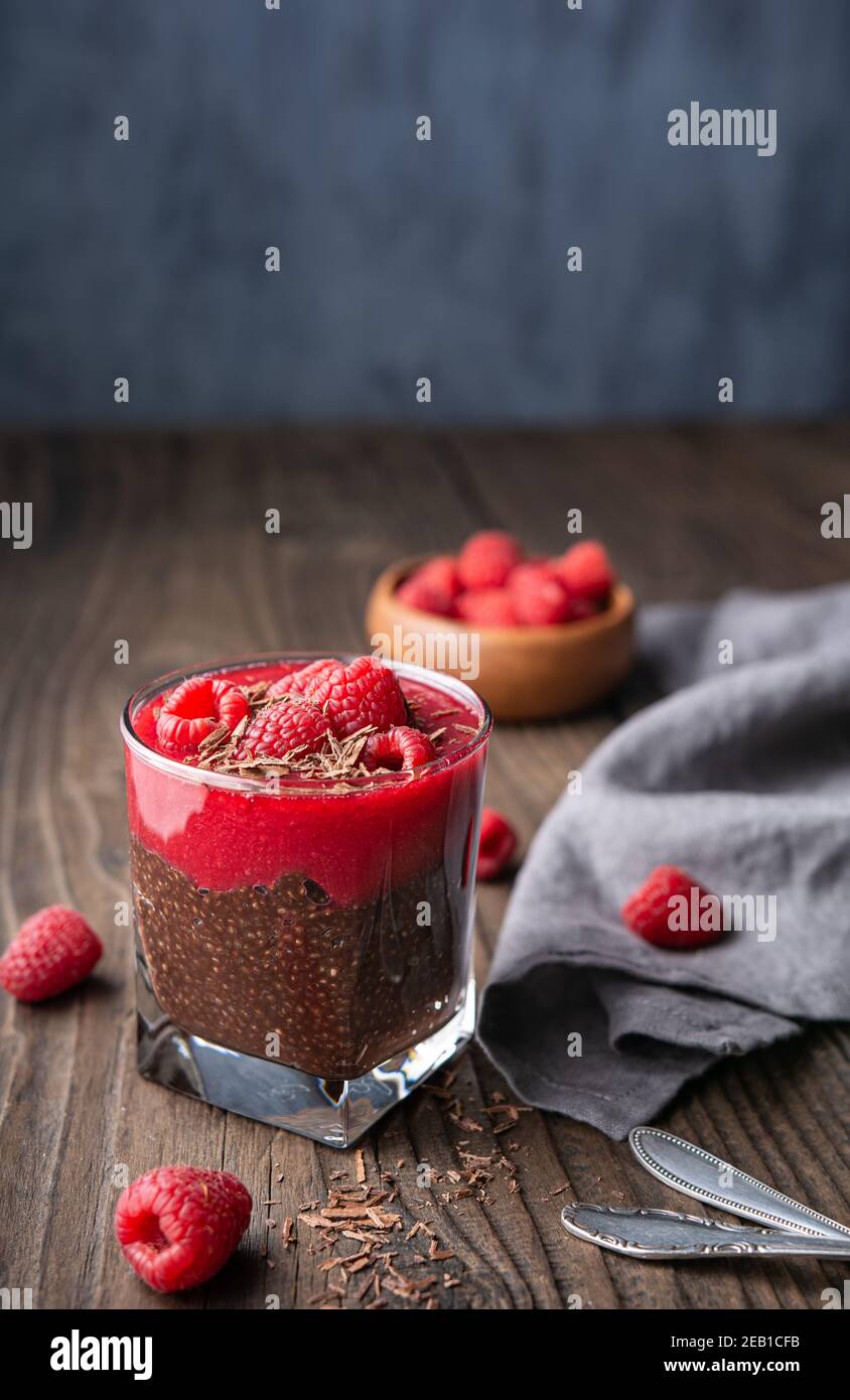 Superfood healthy vegan dessert, dark cocoa chia seed pudding with raspberry puree, topped with fresh berries and chocolate shavings in a glass jar on Stock Photo