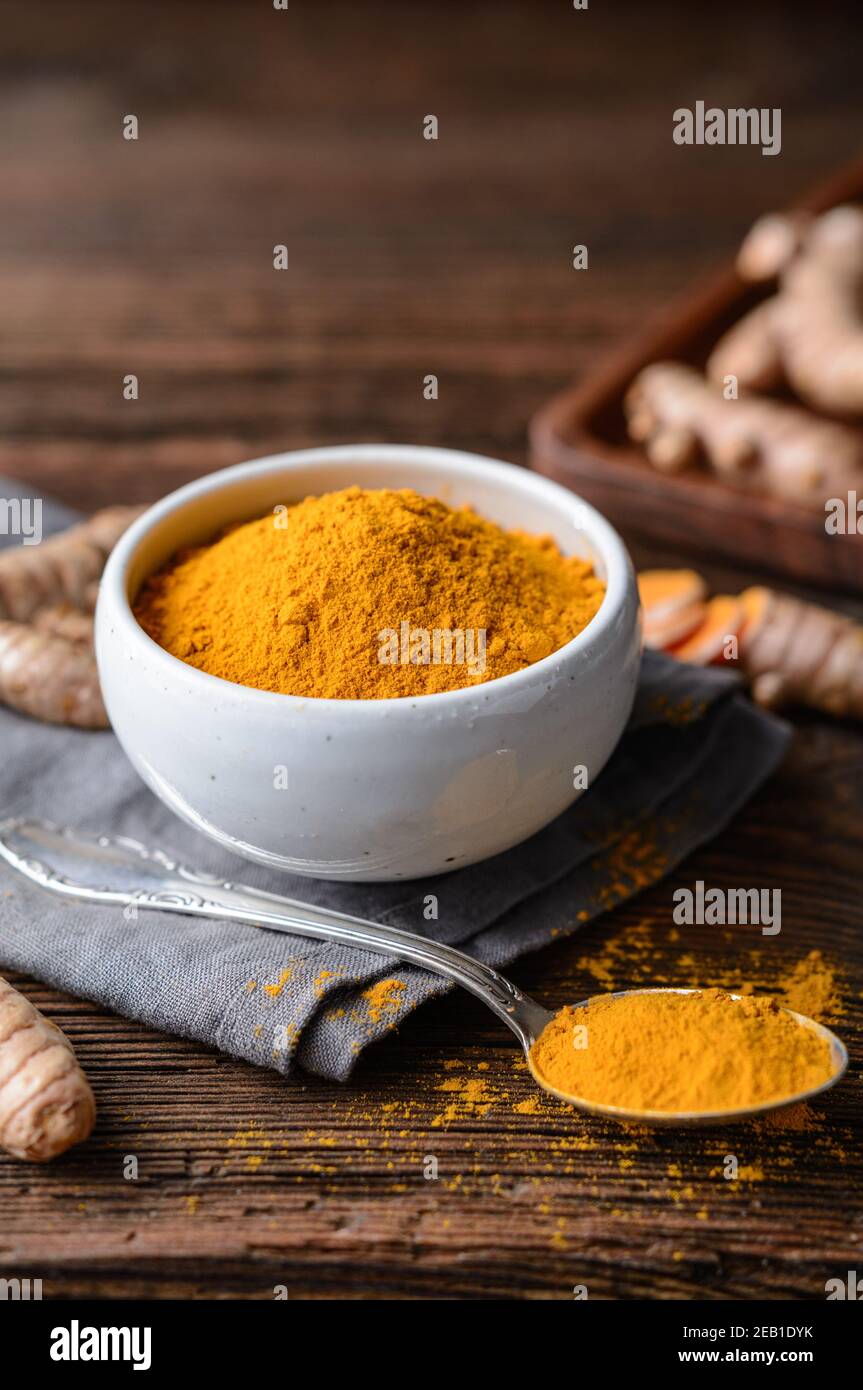 Anti-inflammatory food ingredient, turmeric powder in a ceramic bowl and fresh root on rustic wooden background Stock Photo