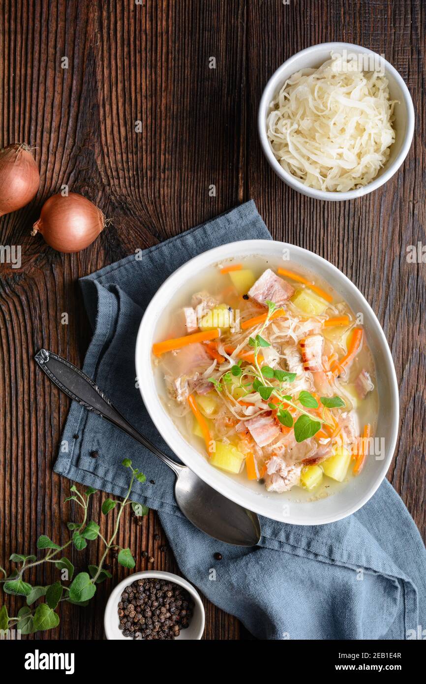 Kapusniak, classic Polish soup made from sauerkraut, pork ribs, smoked bacon, potato, carrot and other vegetable in deep ceramic plate on rustic woode Stock Photo