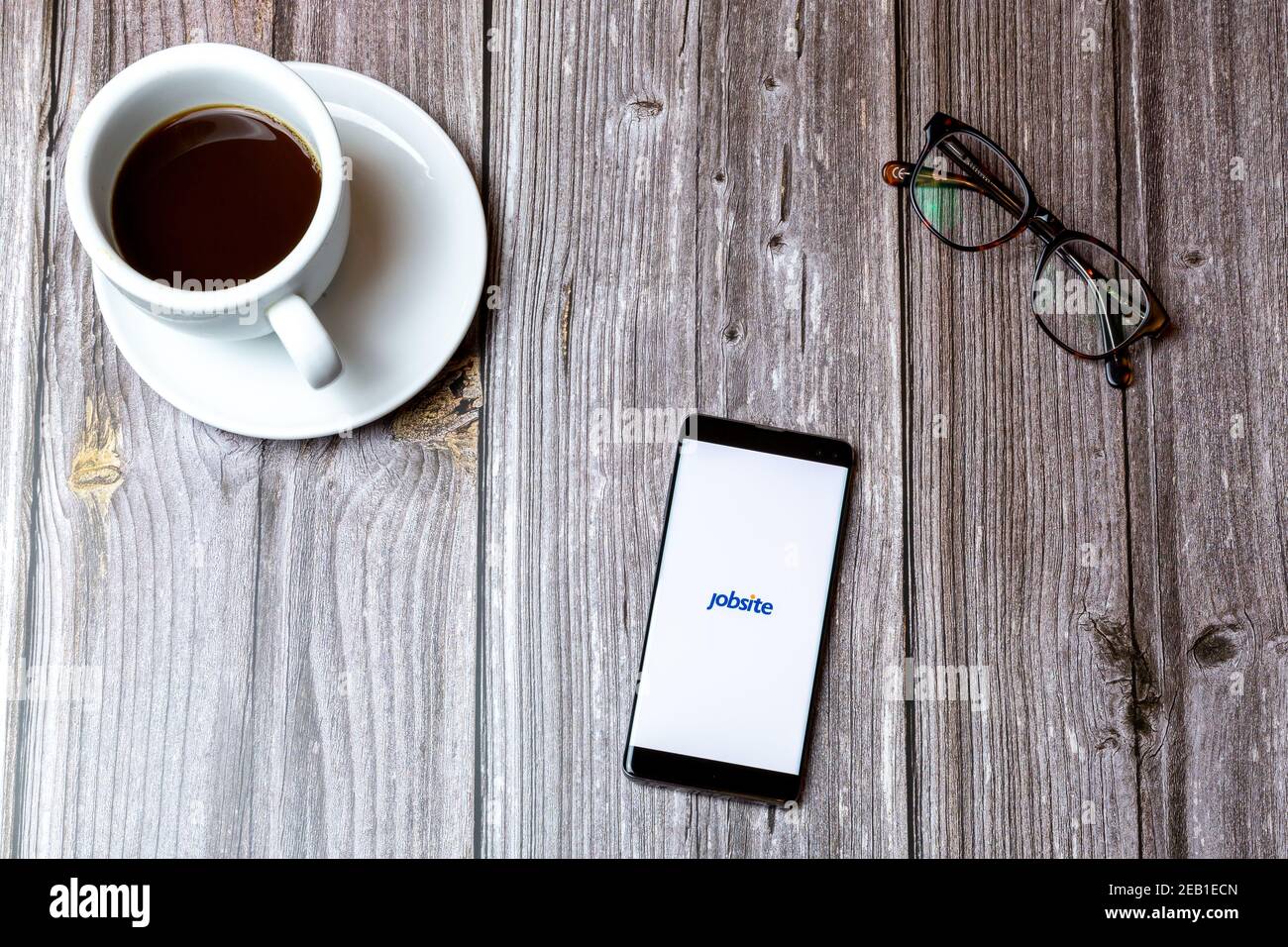 A mobile phone or cell phone laid on a wooden table with the Jobsite app open on screen next to a coffee Stock Photo