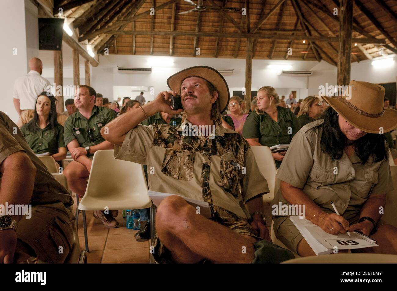 Wildlife ranch manager Berdus Henrico (center) monitors prices during a wildlife auction while speaking by phone with his boss. His partner Estelle Ni Stock Photo