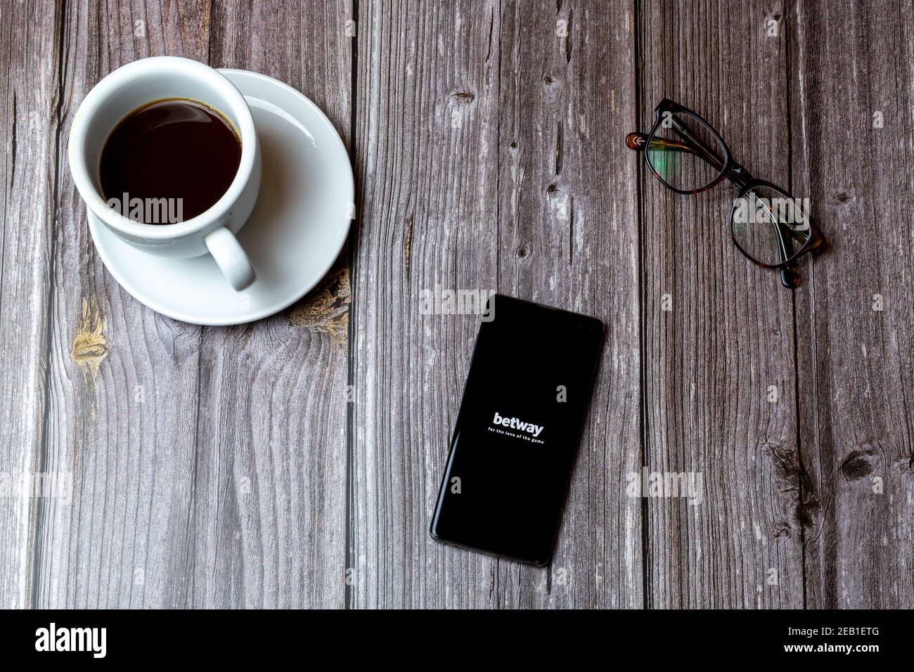 A mobile phone or cell phone laid on a wooden table with the Betway betting app open on screen next to a coffee Stock Photo