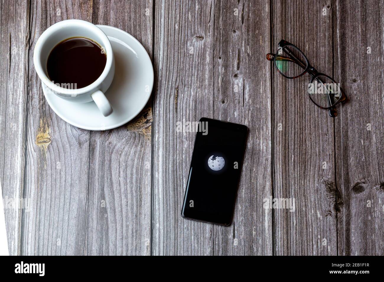 A mobile phone or cell phone laid on a wooden table with the Wikipedia app open on screen next to a coffee Stock Photo