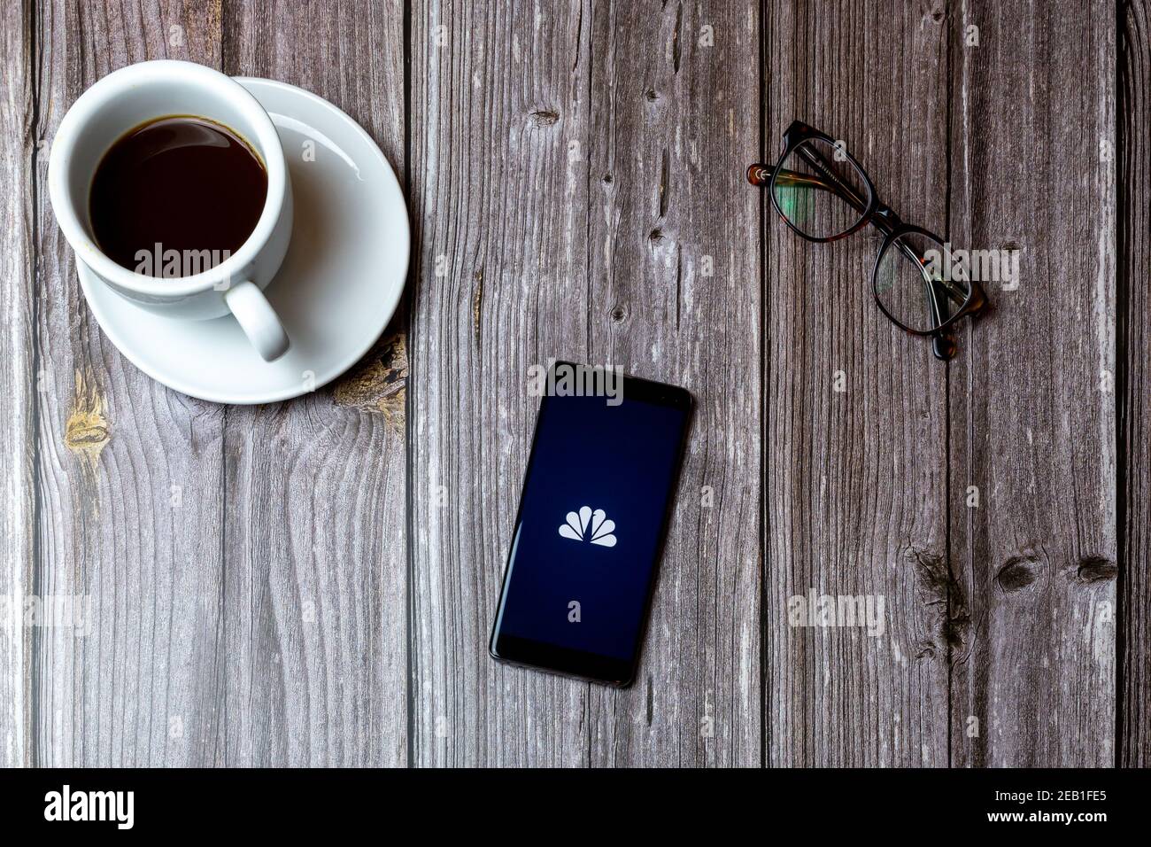 A mobile phone or cell phone laid on a wooden table with the NBC News app open on screen next to a coffee Stock Photo