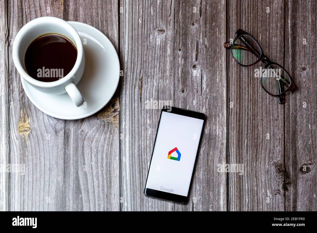 A mobile phone or cell phone laid on a wooden table with the Google home app open on screen next to a coffee Stock Photo