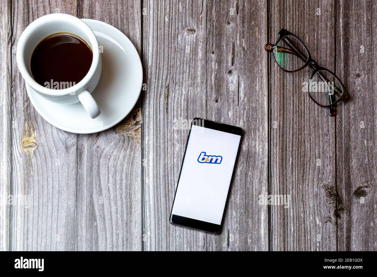 A mobile phone or cell phone laid on a wooden table with the B&M app ...