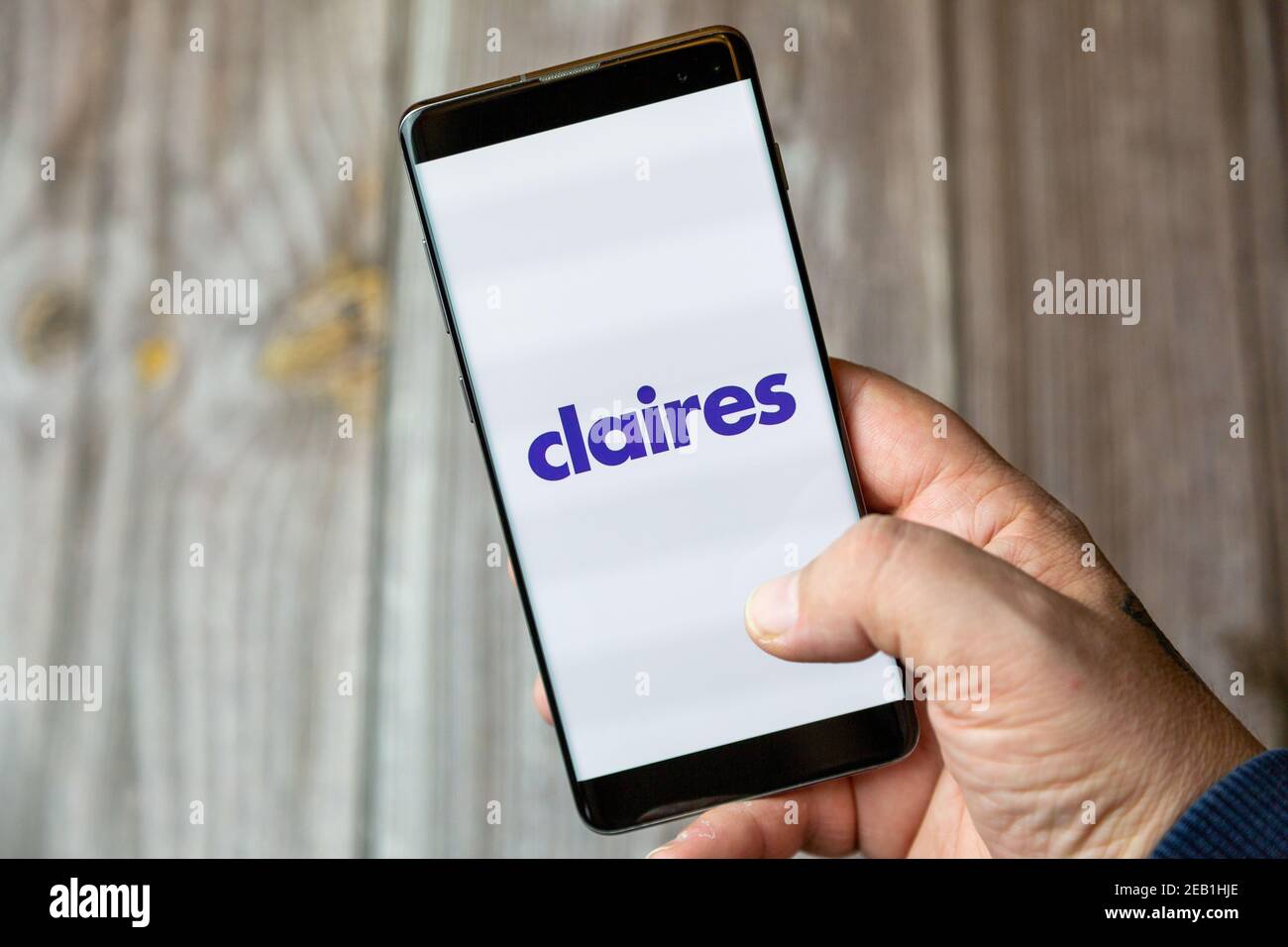A mobile phone or cell phone being held by a hand with the Claires app open on screen Stock Photo