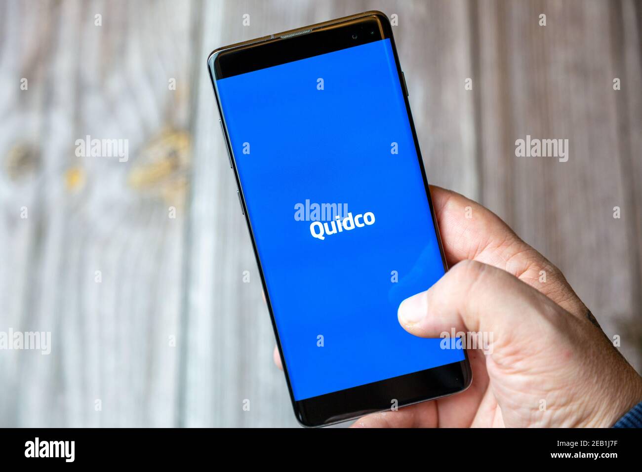 A mobile phone or cell phone being held by a hand with the Quidco app open on screen Stock Photo
