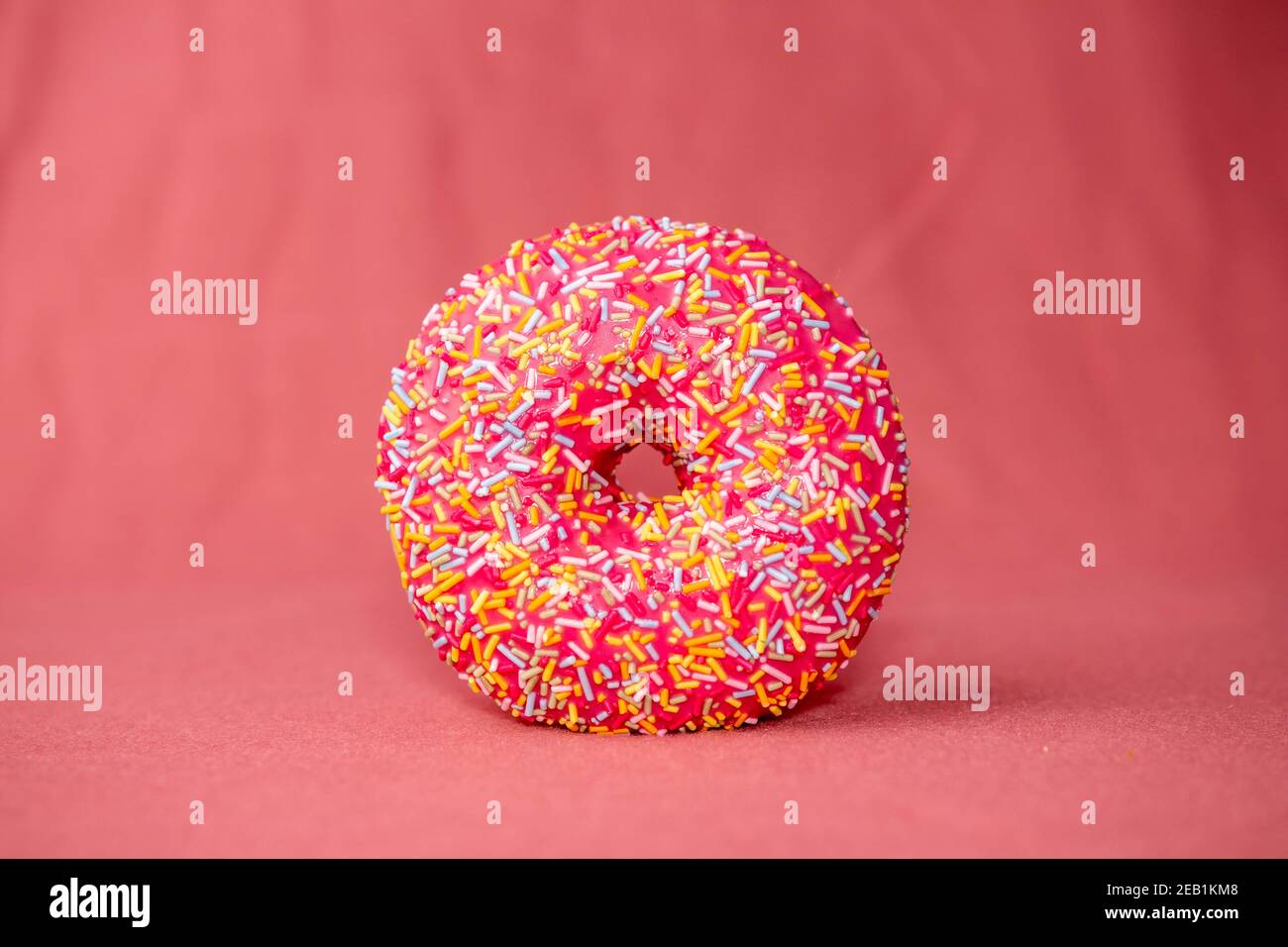 Glazed donut with colorful sprinkles isolated on a pink background ...