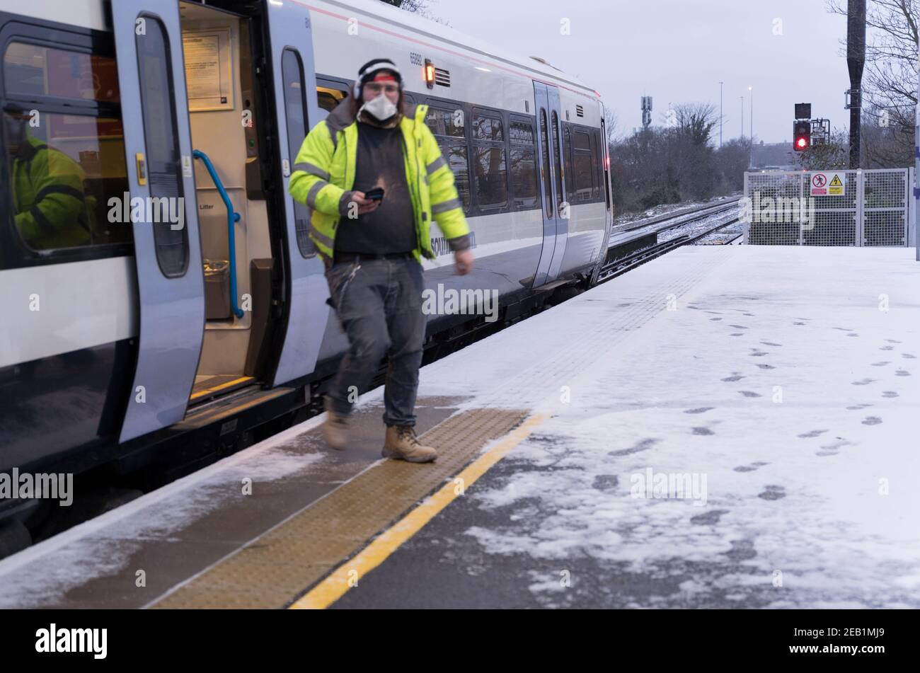a builder in face mask getting off southeastern railway train from work onto platform  covered by heavy snow during storm Darcy week, Kent Stock Photo