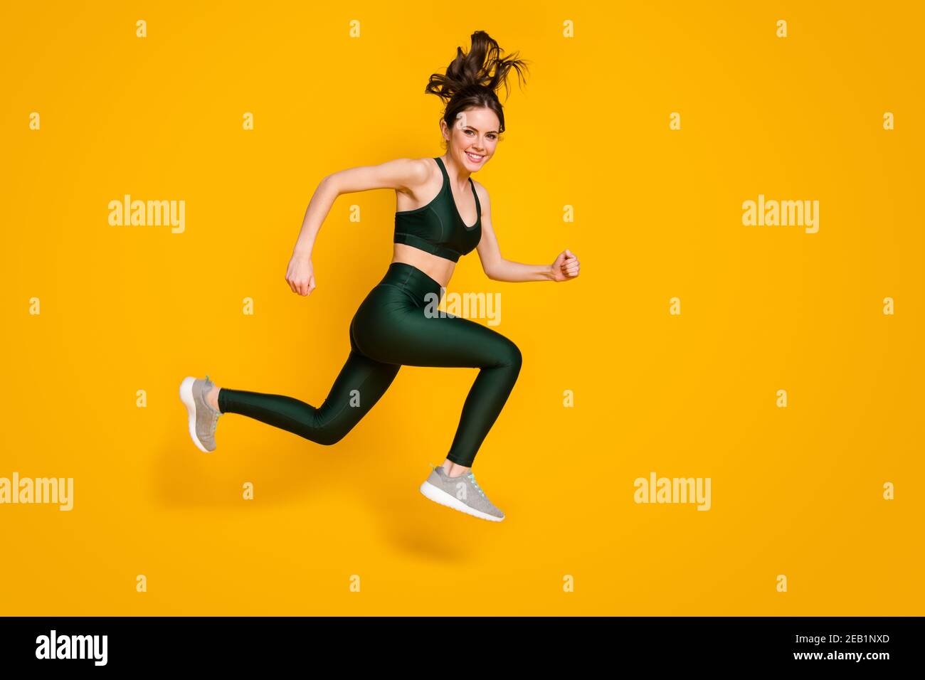 Sportive cheerful lady jump high up jogging marathon participant wear sports suit shoes isolated yellow color background Stock Photo