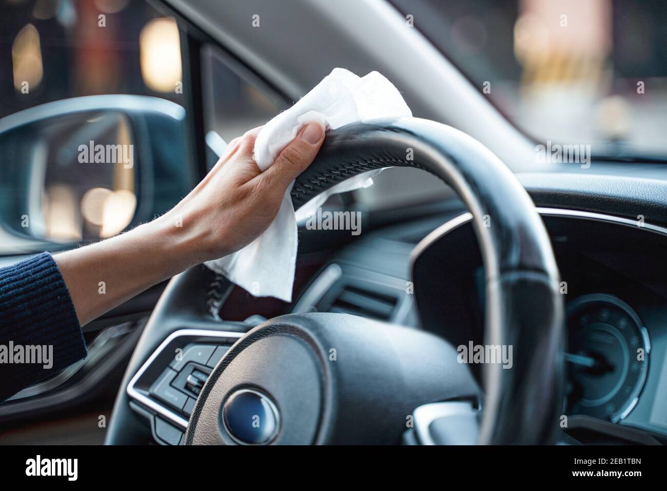 Hands of woman uses disinfectant spray on steering wheel in her car Stock Photo