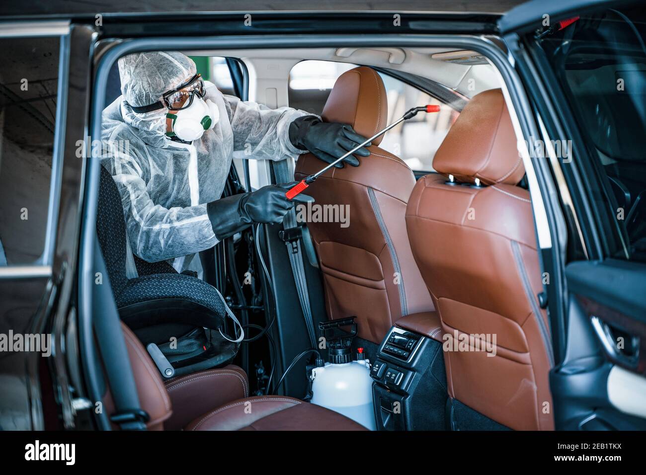 Disinfectant worker in protective mask and suit making disinfection of car seats Stock Photo