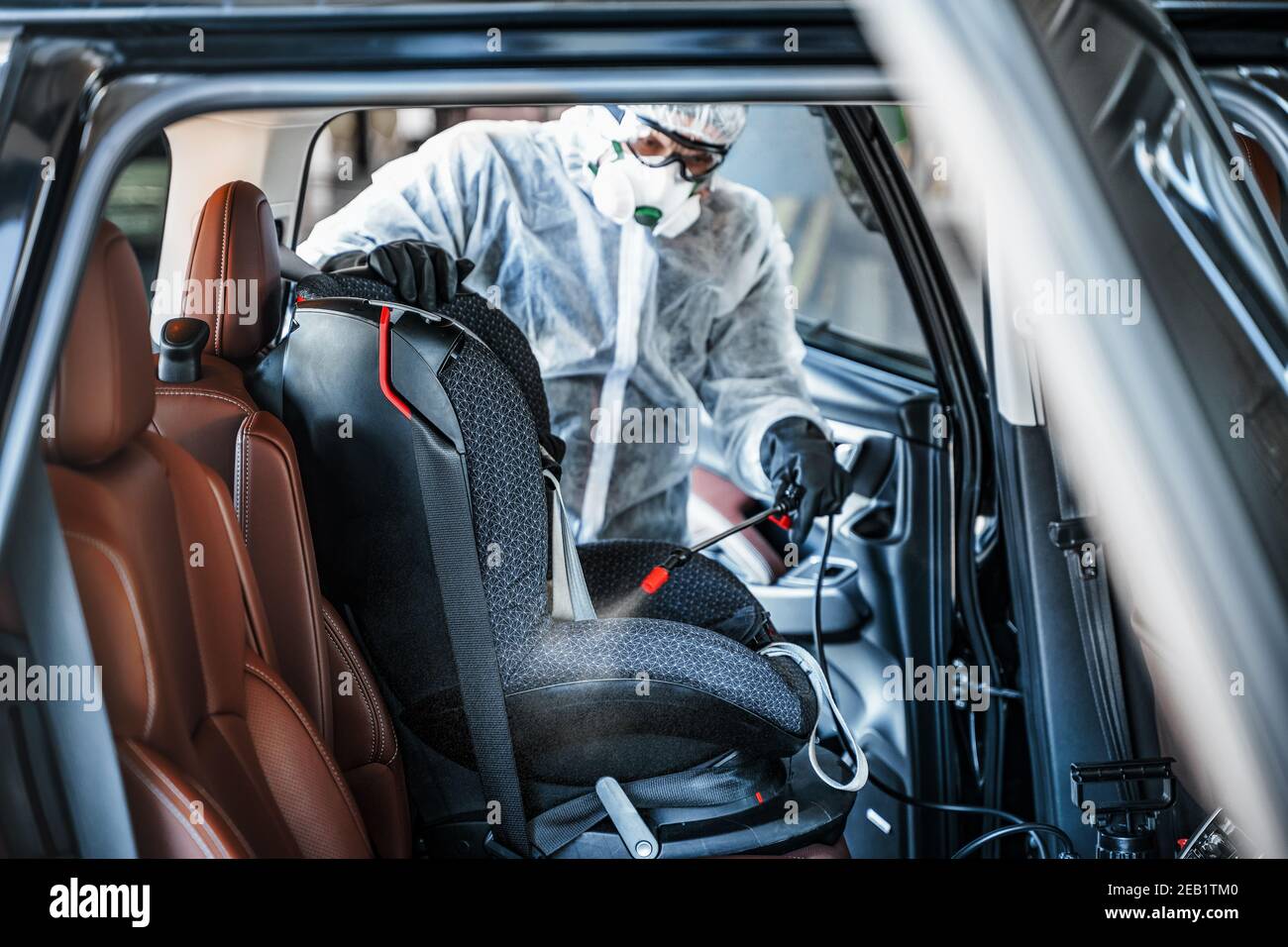 Disinfectant worker in protective mask and suit making disinfection of baby car seat Stock Photo