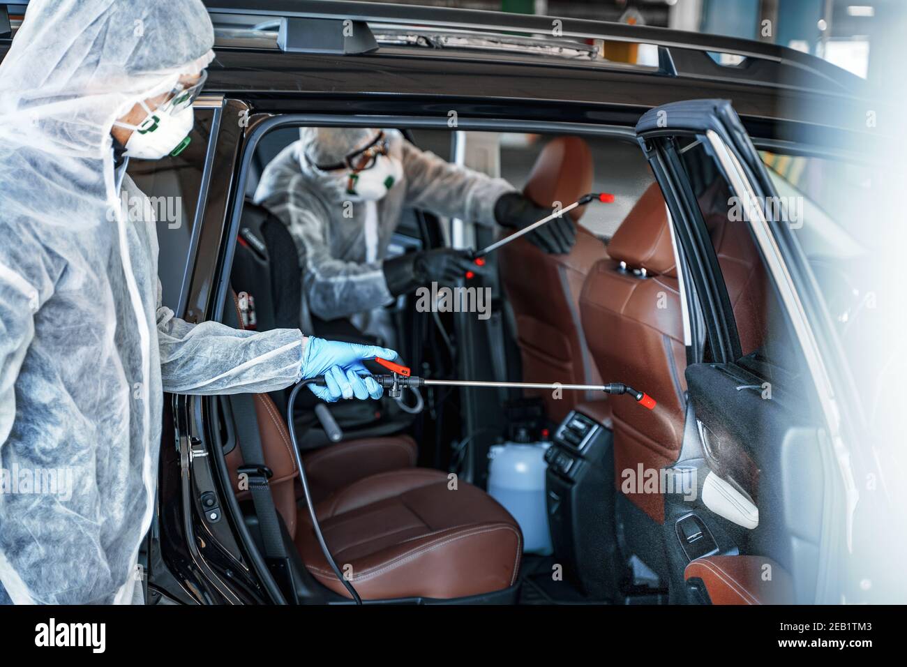 Disinfectant worker in protective masks and suits making disinfection of car seats Stock Photo