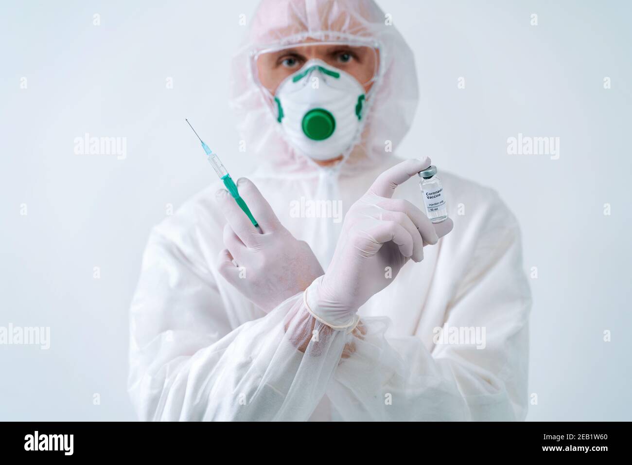 Man in protective suit and mask holds an injection syringe and vaccine. Biological hazard. Stock Photo