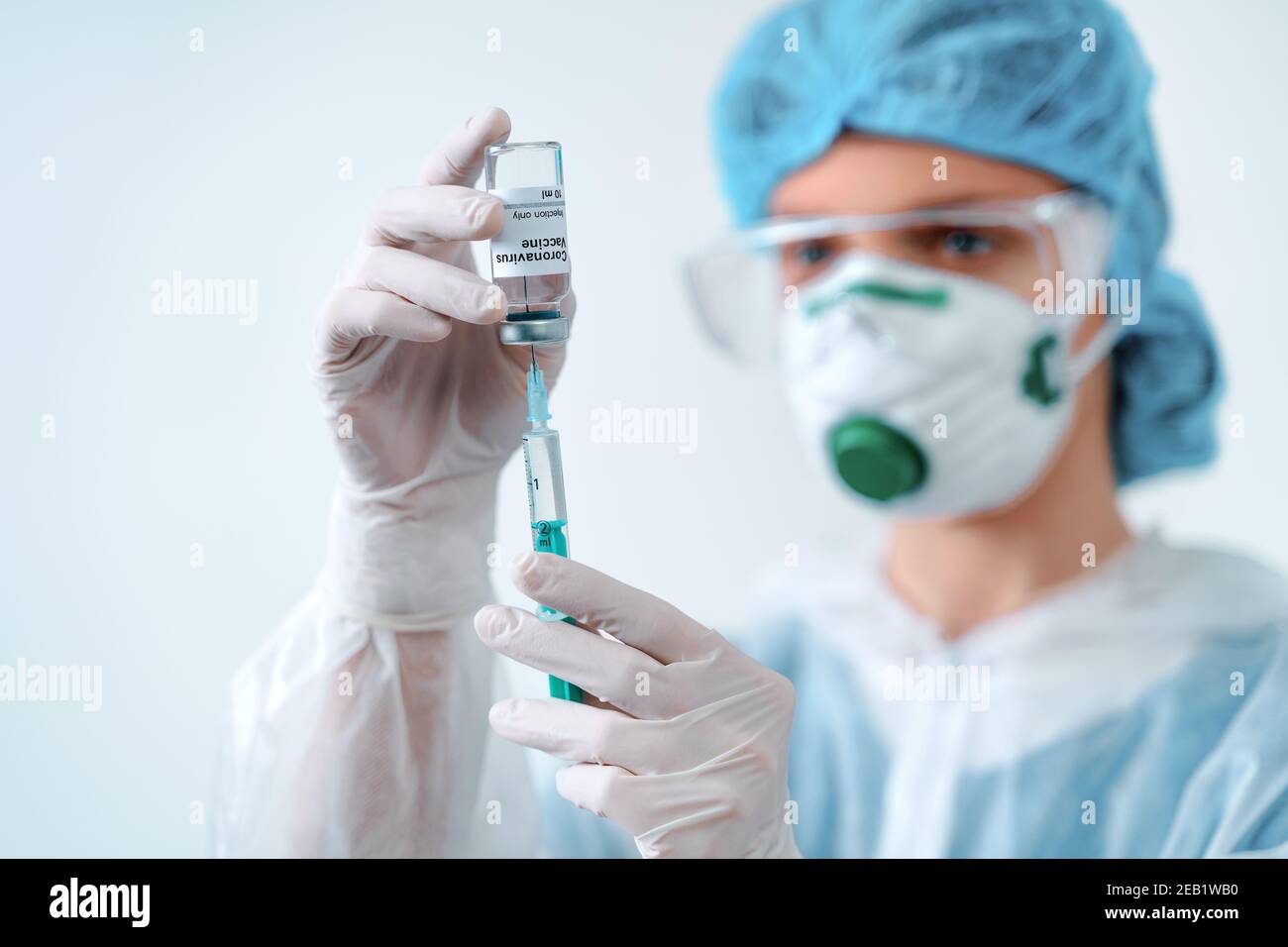 Nurse in protective suit and mask holds an injection syringe and vaccine. Biological hazard. Stock Photo